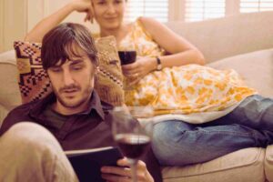 due persone che si rilassano sul divano bevendo un bicchiere di vino e leggendo un libro