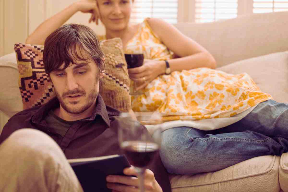 due persone che si rilassano sul divano bevendo un bicchiere di vino e leggendo un libro